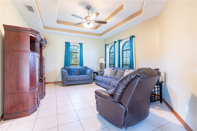 tiled living room with ceiling fan and a raised ceiling