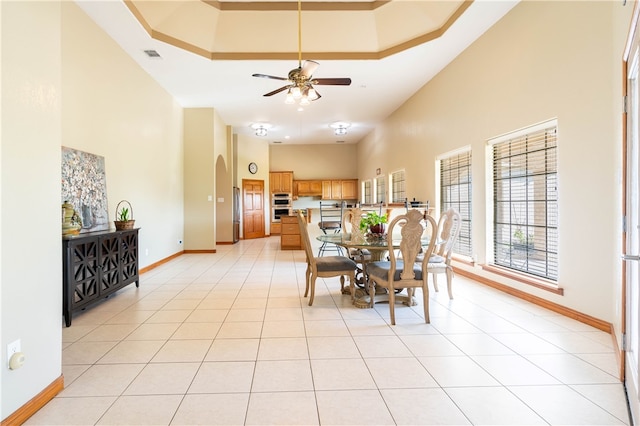 tiled dining space featuring a tray ceiling, ceiling fan, and a towering ceiling