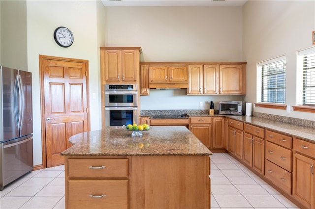 kitchen featuring stainless steel appliances, a towering ceiling, light tile patterned flooring, and a center island