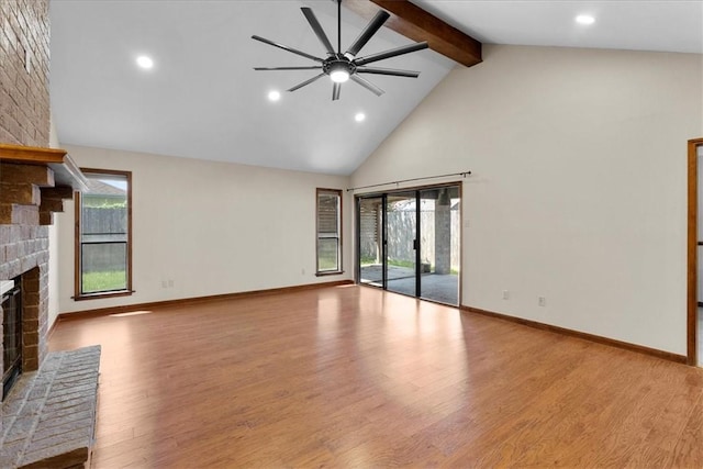 unfurnished living room with a brick fireplace, a healthy amount of sunlight, beam ceiling, and wood finished floors