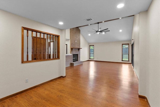 unfurnished living room featuring lofted ceiling, wood finished floors, a ceiling fan, baseboards, and a brick fireplace