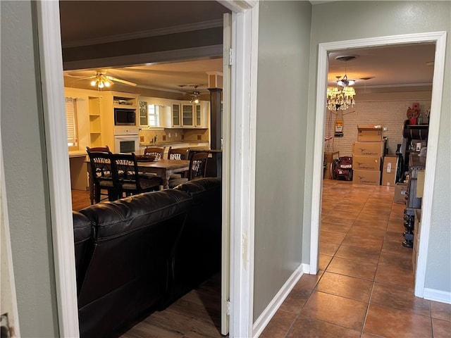 hallway with baseboards, brick wall, crown molding, and tile patterned flooring