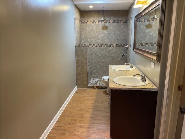 full bathroom with a sink, baseboards, tiled shower, and wood finished floors