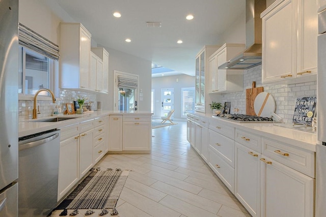 kitchen with a sink, a peninsula, wall chimney exhaust hood, recessed lighting, and appliances with stainless steel finishes