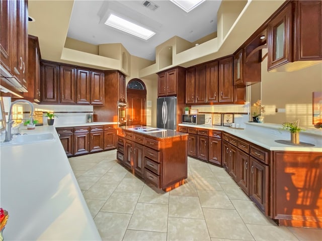 kitchen with stainless steel appliances, a kitchen island, light tile patterned floors, decorative backsplash, and sink