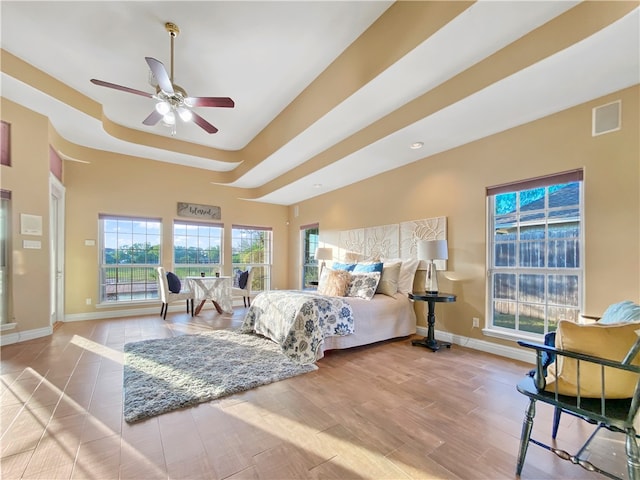 bedroom featuring ceiling fan, light wood-type flooring, and a tray ceiling