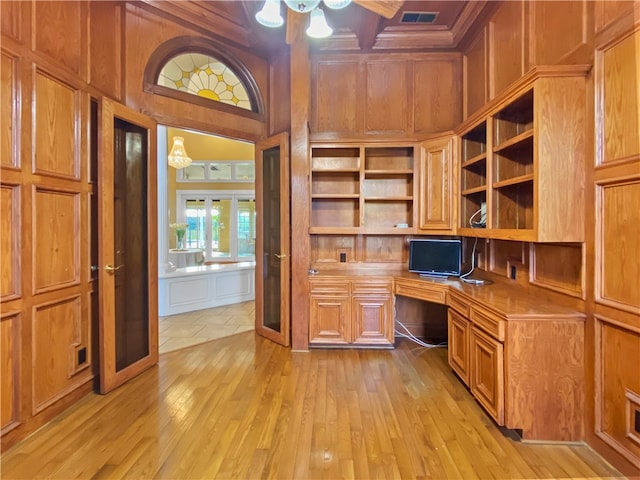 unfurnished office featuring light hardwood / wood-style floors, wooden walls, and built in desk