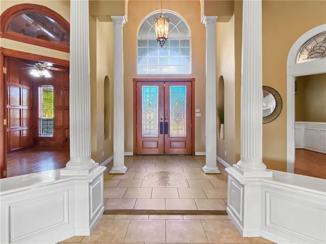 foyer with a towering ceiling, light tile patterned floors, french doors, and decorative columns