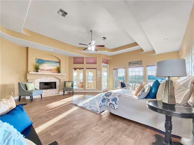 bedroom featuring hardwood / wood-style flooring, ceiling fan, a raised ceiling, and a premium fireplace