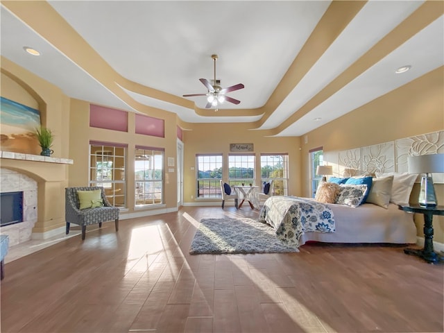 bedroom with a high end fireplace, hardwood / wood-style flooring, ceiling fan, and a raised ceiling