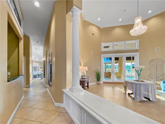 hall with a chandelier, light tile patterned floors, a high ceiling, and decorative columns