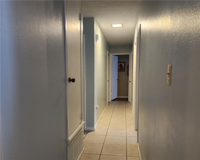 hallway featuring light tile patterned floors, baseboards, visible vents, and a textured ceiling