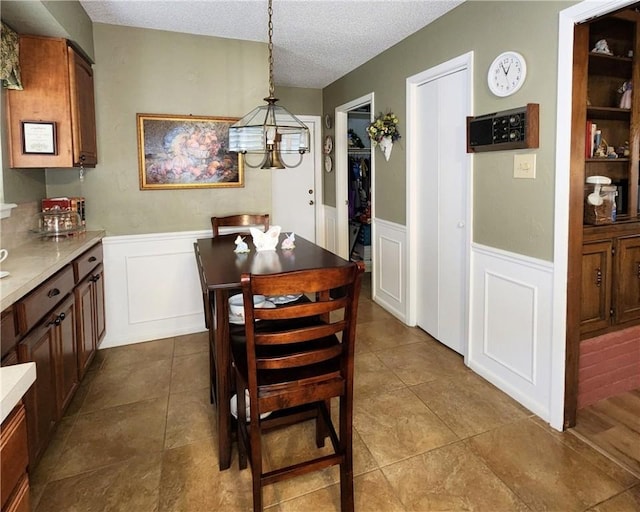 dining room featuring a wainscoted wall, a textured ceiling, and dark tile patterned flooring