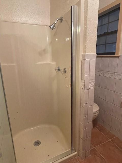 bathroom featuring a shower, tile walls, tile patterned floors, and toilet