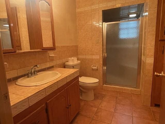 bathroom featuring tile walls, vanity, toilet, a shower with door, and tile patterned floors