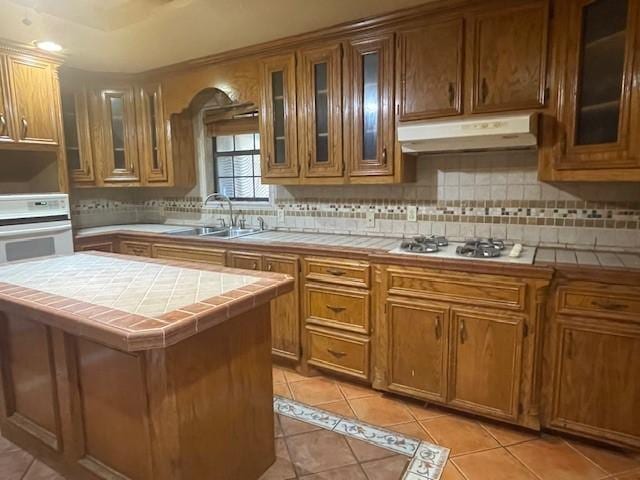 kitchen featuring sink, tile counters, white gas stovetop, and a kitchen island