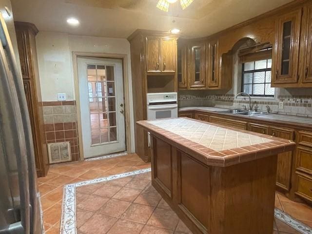 kitchen featuring a kitchen island, tile countertops, sink, oven, and light tile patterned floors