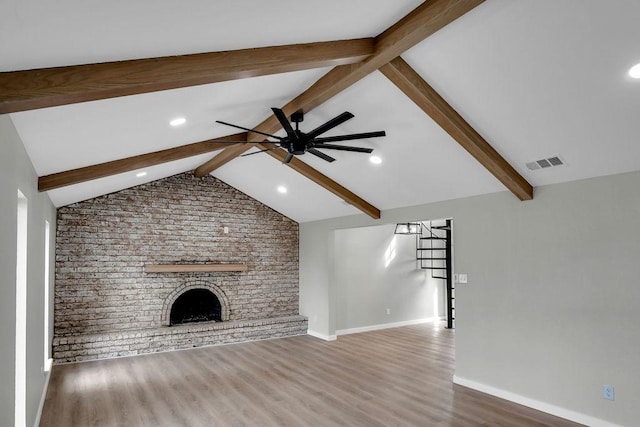 unfurnished living room with vaulted ceiling with beams, visible vents, a brick fireplace, ceiling fan, and wood finished floors