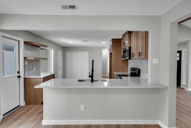 kitchen featuring electric range, brown cabinets, a peninsula, light countertops, and a sink