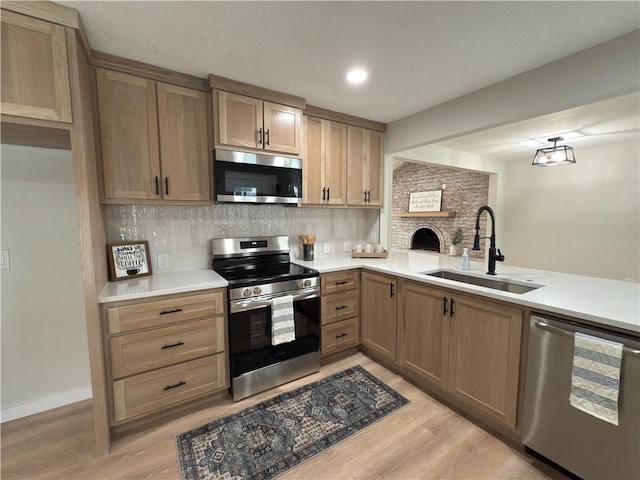 kitchen with stainless steel appliances, tasteful backsplash, light countertops, a sink, and light wood-type flooring