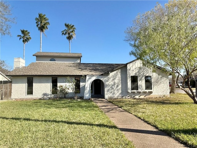 view of front of house featuring roof with shingles, brick siding, a chimney, and a front yard