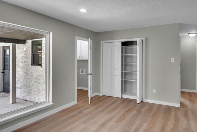 unfurnished bedroom featuring a textured ceiling, light wood finished floors, a closet, and baseboards