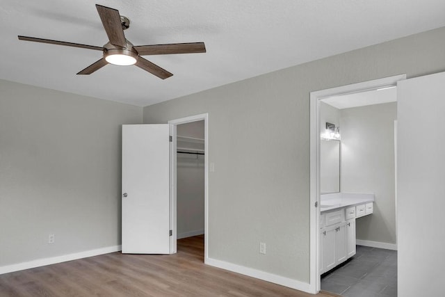 unfurnished bedroom with ensuite bathroom, a spacious closet, ceiling fan, light wood-type flooring, and a closet