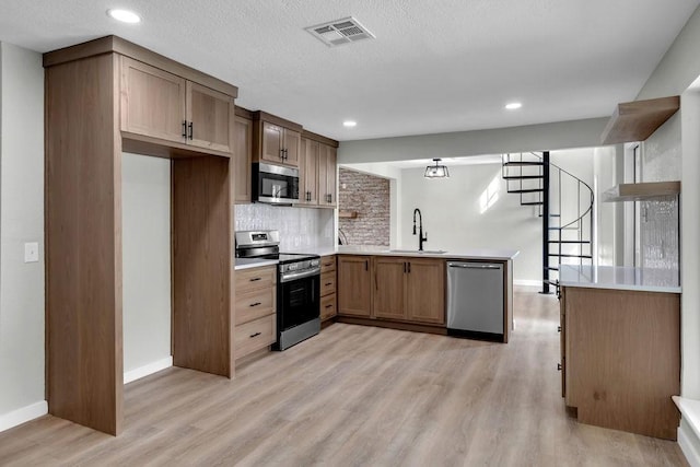 kitchen with tasteful backsplash, sink, light hardwood / wood-style floors, kitchen peninsula, and stainless steel appliances