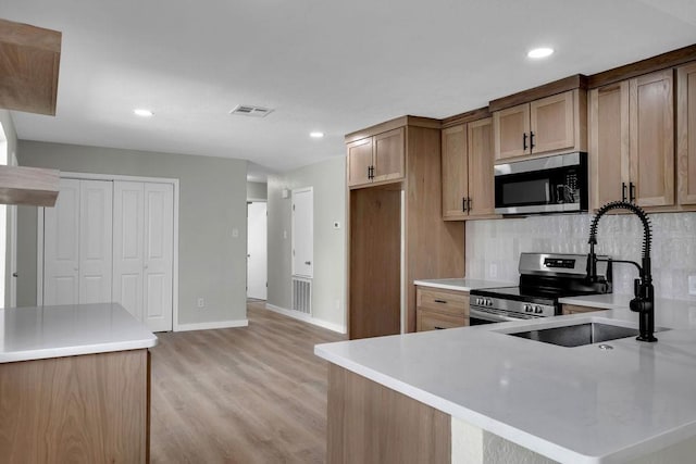 kitchen with sink, tasteful backsplash, light hardwood / wood-style flooring, kitchen peninsula, and stainless steel appliances