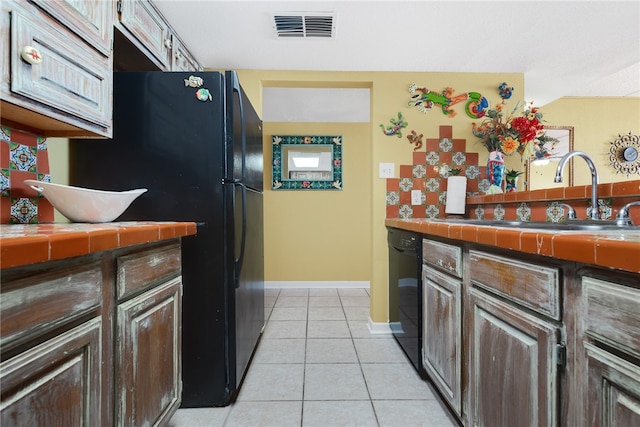 kitchen with sink, black appliances, light tile patterned floors, dark brown cabinets, and tile counters