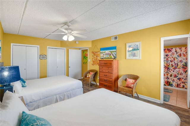 bedroom with a textured ceiling, hardwood / wood-style flooring, ensuite bathroom, ceiling fan, and multiple closets