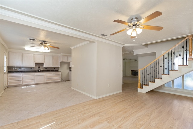 unfurnished living room with ceiling fan, sink, ornamental molding, and light hardwood / wood-style flooring