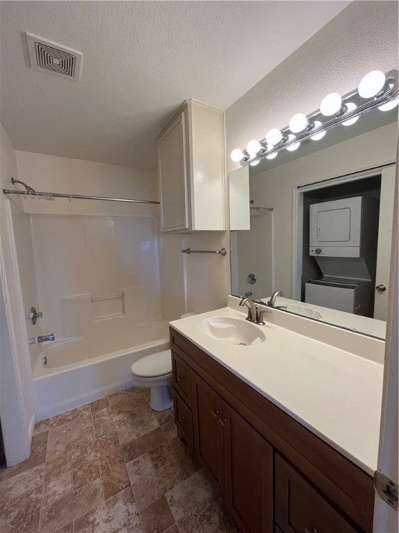 full bathroom featuring stacked washer / drying machine, a textured ceiling, vanity, bathtub / shower combination, and toilet