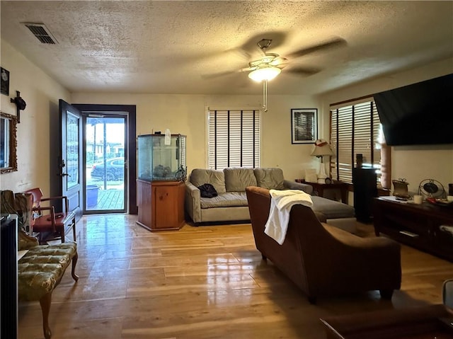 living room with a textured ceiling, visible vents, light wood-style floors, and a ceiling fan