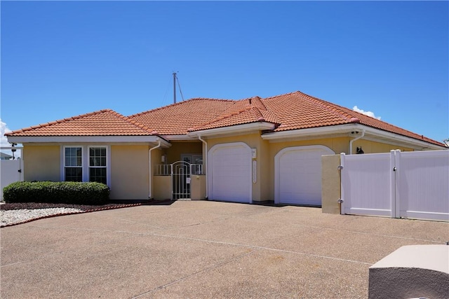 mediterranean / spanish-style house featuring concrete driveway, a tiled roof, an attached garage, a gate, and stucco siding