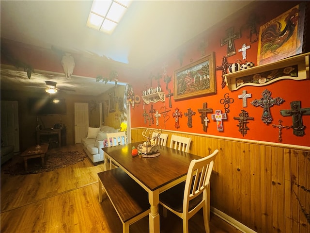 dining area with wood walls, wood-type flooring, and ceiling fan