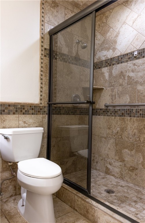 bathroom with tile patterned flooring, toilet, a shower with door, and tile walls