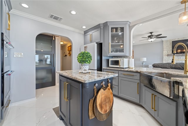 kitchen with light stone counters, ceiling fan, a kitchen island, crown molding, and gray cabinets