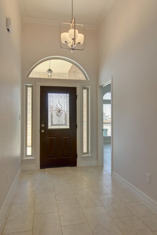 tiled foyer entrance with a chandelier, ornamental molding, and a towering ceiling