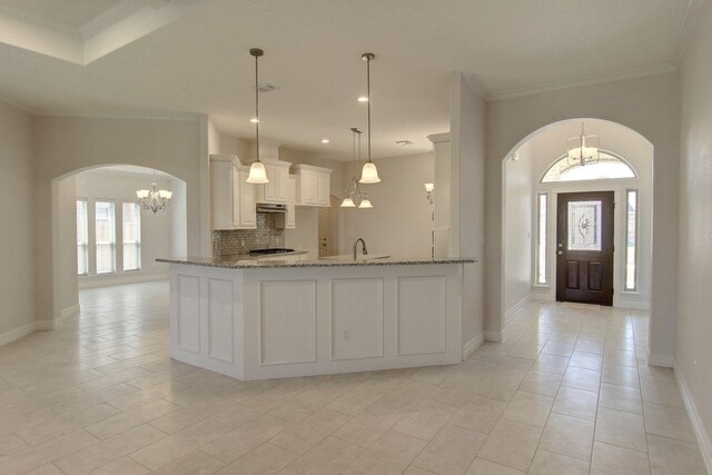 kitchen with light stone counters, kitchen peninsula, hanging light fixtures, tasteful backsplash, and white cabinetry