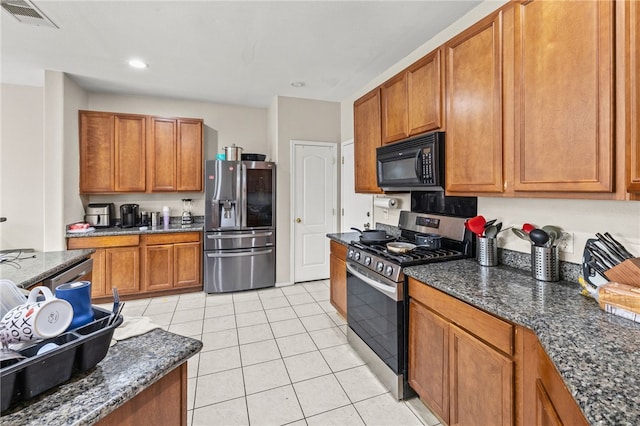 kitchen featuring light tile patterned floors, stainless steel appliances, visible vents, brown cabinetry, and dark stone counters