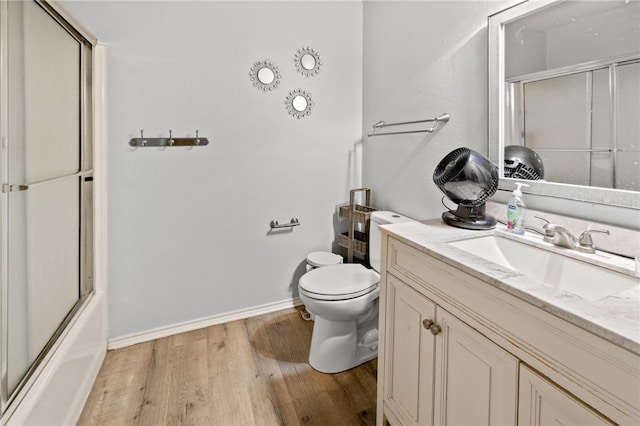 bathroom with baseboards, toilet, shower / bath combination with glass door, wood finished floors, and vanity