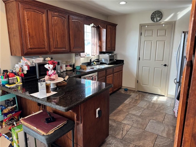 kitchen with sink, stainless steel appliances, dark stone countertops, kitchen peninsula, and a breakfast bar