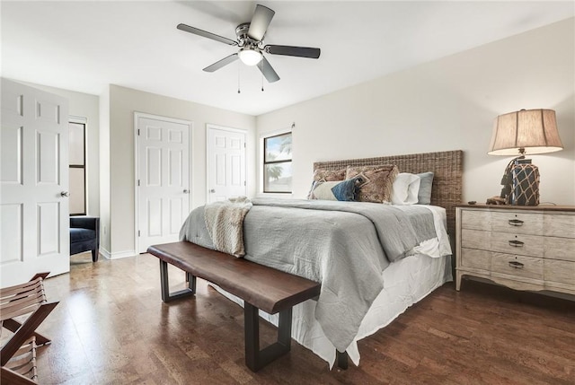 bedroom featuring baseboards, dark wood finished floors, two closets, and a ceiling fan