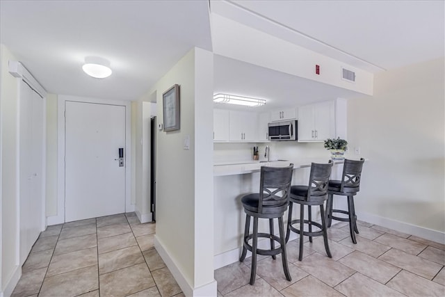 kitchen with white cabinets, light tile patterned flooring, a kitchen bar, and kitchen peninsula