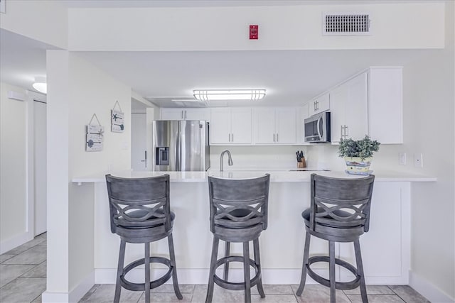 kitchen featuring stainless steel appliances, kitchen peninsula, light tile patterned floors, a breakfast bar, and white cabinetry