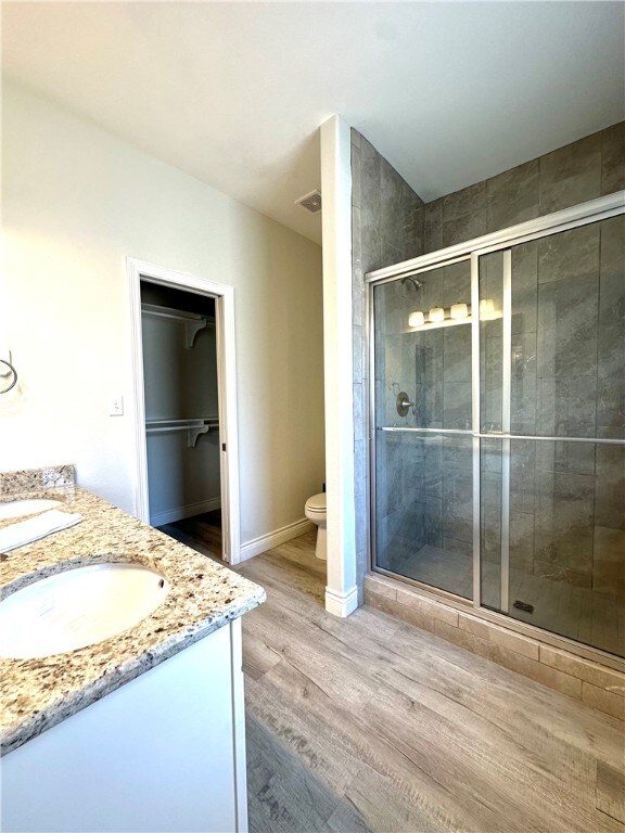 bathroom featuring toilet, vanity, wood-type flooring, and a shower with shower door