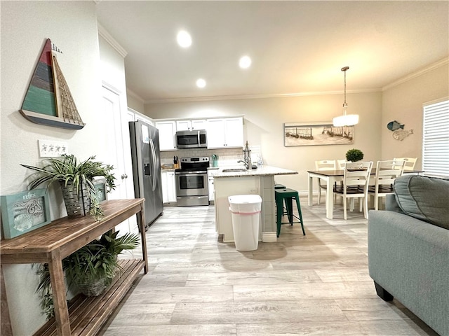 kitchen with white cabinetry, appliances with stainless steel finishes, a kitchen bar, hanging light fixtures, and light hardwood / wood-style flooring