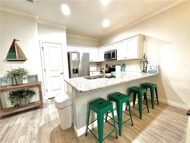 kitchen with light hardwood / wood-style floors, white cabinets, decorative backsplash, ornamental molding, and appliances with stainless steel finishes