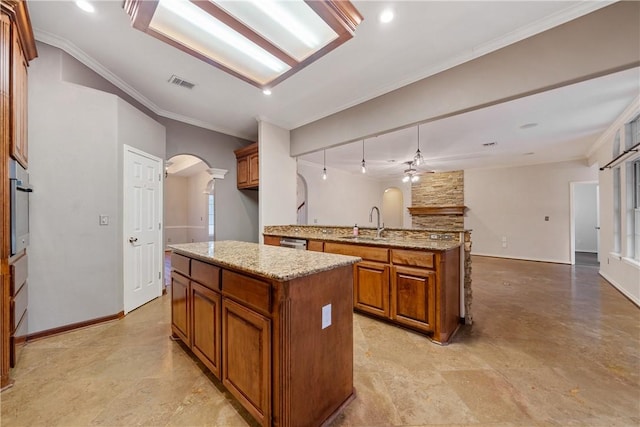 5609 Leicester Dr, Corpus Christi, TX 78414 - kitchen featuring arched walkways, brown cabinetry, open floor plan, a center island, and light stone counters